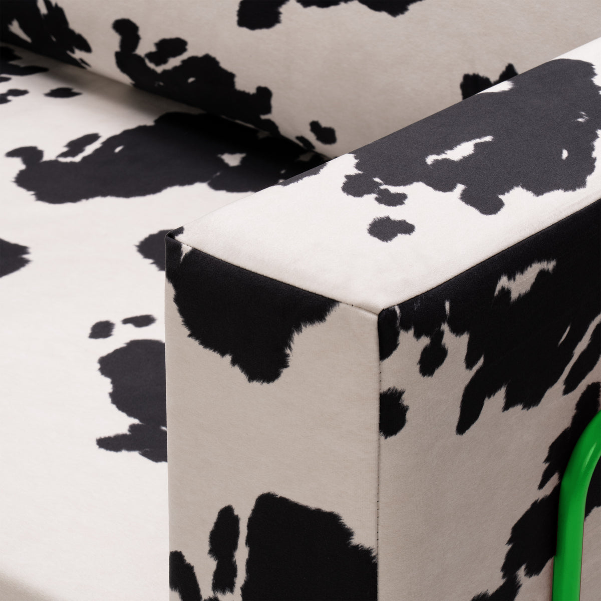 Flow Cow sofa bed in black-and-white cow print fabric with a green metal frame, close-up of the armrest corner