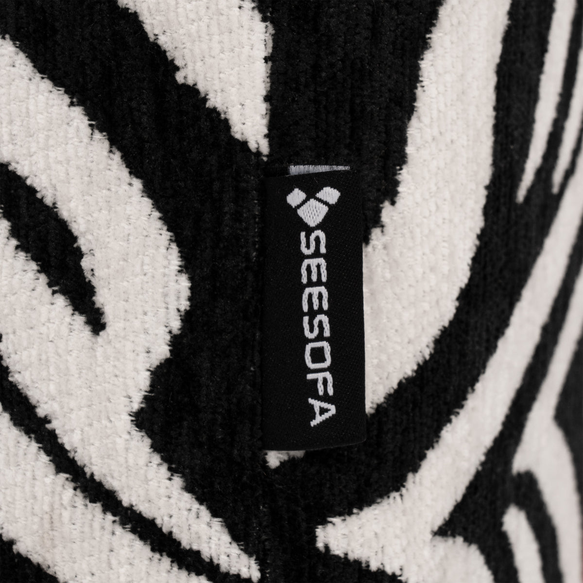 Flow Zebra sovesofa i sort-hvidt zebramønster med rødt metalstel, nærbillede af zebrastoffet med Seesofa-mærket