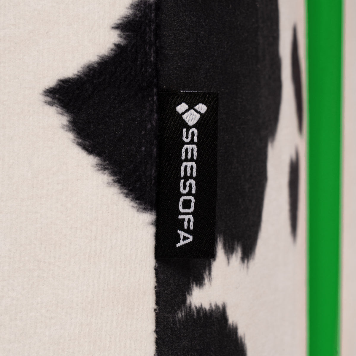 Flow Cow sofa bed in black-and-white cow print fabric with a green metal frame, close-up of the cow print fabric with the Seesofa label