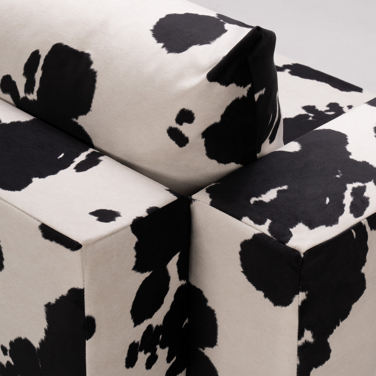 Flow Cow sofa bed in black-and-white cow print fabric with a green metal frame, close-up of the back cushion and armrest