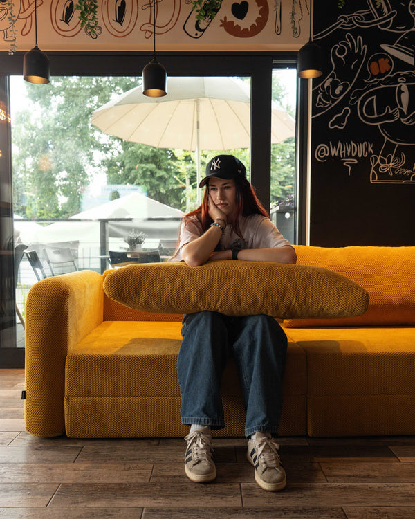 Frau sitzt auf einem ockerfarbenen Flowy Schlafsofa in einem Café