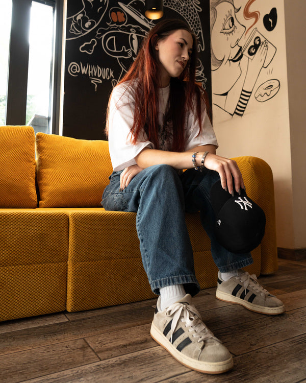 Junge Frau sitzt auf einem ockerfarbenen Flowy Schlafsofa in einem Café