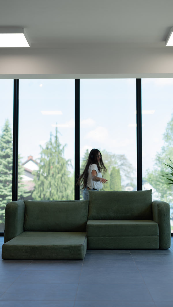 Dunkelgrünes Flowy Schlafsofa an einem großen Fenster