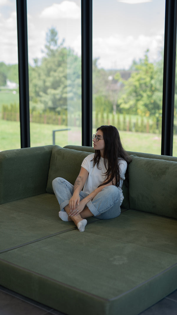 Frau sitzt auf einem dunkelgrünen Flowy Schlafsofa am Fenster