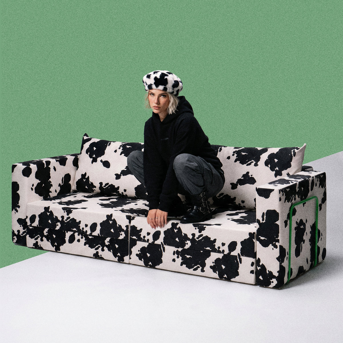 Person sitting on a Flow Cow sofa bed in black-and-white cow print fabric